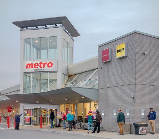 A photograph of people lined-up outside of Metro in fall time, some are masked.