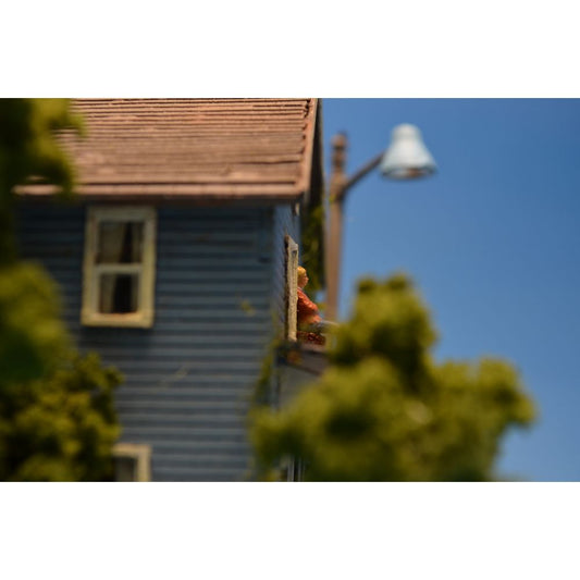 Photograph of a miniature diorama, featuring a sideview of a house with a pregnant woman standing on a balcony.